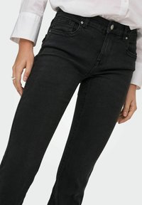 Sorte denim jeans med en tætsiddende design, der har forlommer og lynlås. Stoffet har en glat tekstur og let slidte områder.