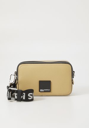 Sárga műbőr keresztpántos táska cipzárral, téglalap alakú, fekete logóval és eltávolítható fekete pánttal, amelyen fehér szöveg található.