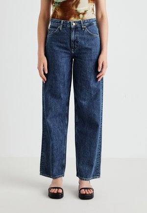Jeans in denim scuro a gamba larga con vita alta, dotati di cinque tasche, tessuto misto e leggera scoloritura sulle gambe. Sandali neri visibili.