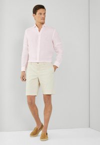 Lyserød linned skjorte med knapper, beige shorts og brune slip-on sko. Korte ærmer, klassisk krave, neutral farvepalette.