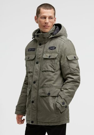 Green parka jacket with a hood, featuring multiple front pockets, button closures, and black accents. Textured fabric with a matte finish.
