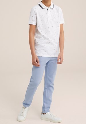 Polo blanc avec petits motifs bleus et rouges, bordure de col noire, associé à un pantalon fuselé bleu clair et des baskets blanches.