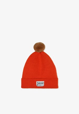 Bonnet en tricot rouge avec une texture côtelée, ornée d'un pompon en fausse fourrure marron sur le dessus et d'un patch logo Timberland blanc sur le revers.