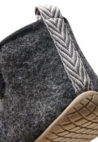 Gros plan sur une pantoufle en laine gris foncé avec semelle texturée et languette en tissu gris à motif chevron.
