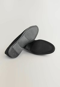 Schwarze Wildleder-Slipper mit Gummisohlen, die eine glatte Textur und kontrastierende graue Akzente an der Unterseite aufweisen.