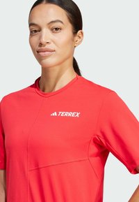 Röd kortärmad prestandatröja i ventilerande material, med sömdetaljer och en framträdande vit "TERREX"-logotyp på bröstet.