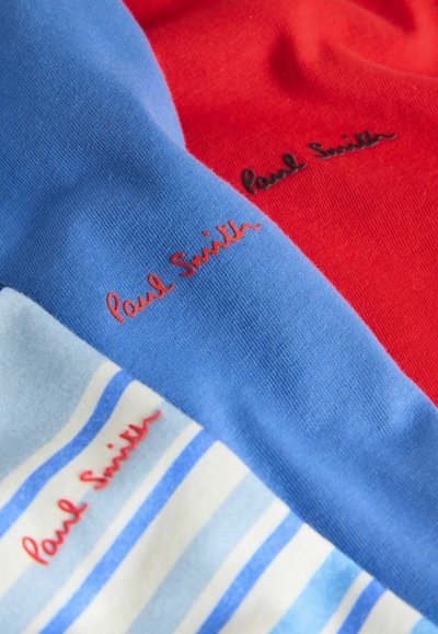 Gros plan sur trois vêtements pliés aux rayures rouge, bleue et bleu clair, chacun avec "Paul Smith" brodé en fil contrastant.