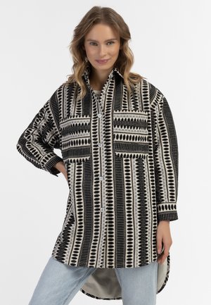 Cămașă cu model negru și crem, cu guler, mâneci lungi, două buzunare pe piept și un tiv mai lung la spate. Material texturat.