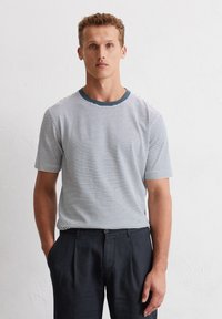 T-shirt à rayures à manches courtes blanc et marine avec un col rond marine, associé à un pantalon noir ajusté ; texture de tissu lisse.