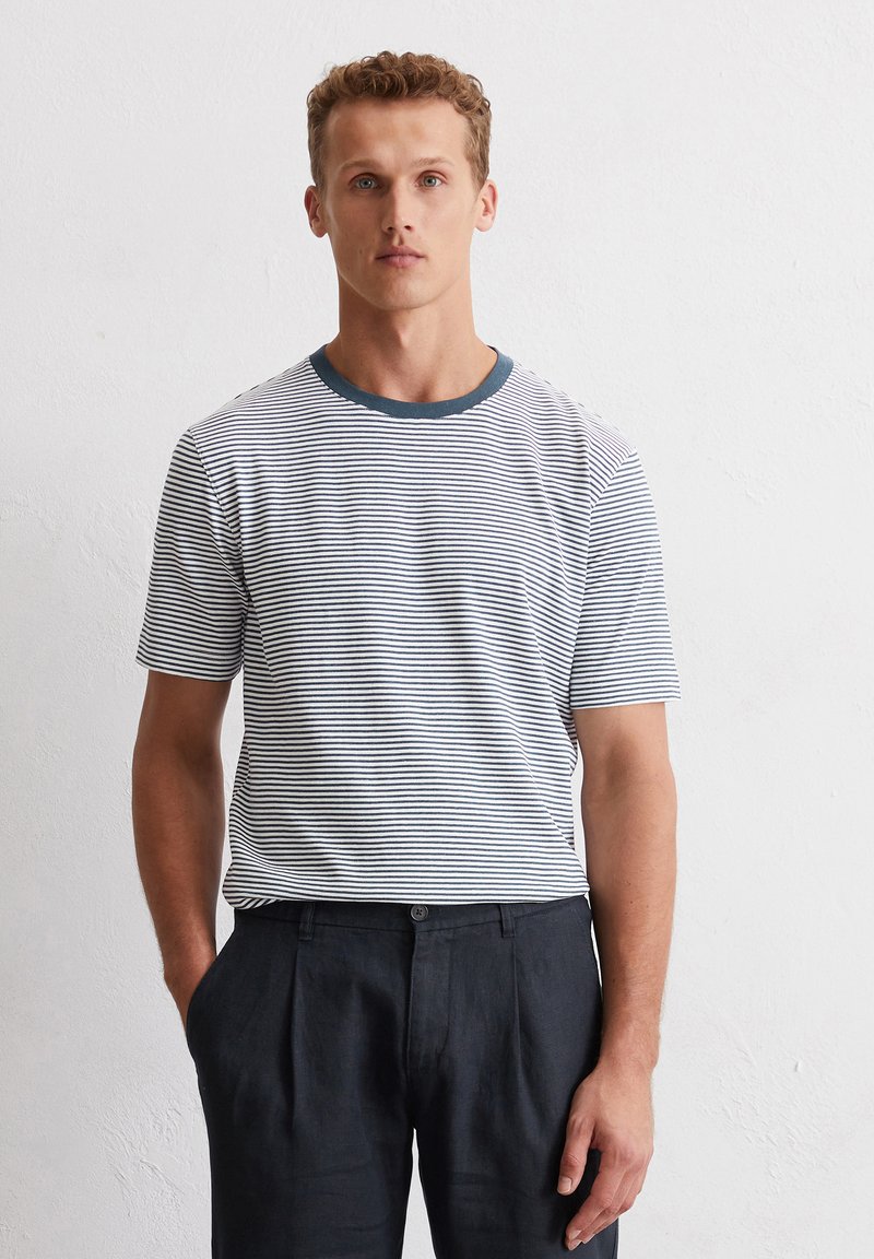 T-shirt à rayures à manches courtes blanc et marine avec un col rond marine, associé à un pantalon noir ajusté ; texture de tissu lisse.