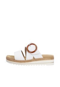 White slide sandals with two wide straps, featuring a large brown circular accent. Textured sole with a layered, woven appearance.
