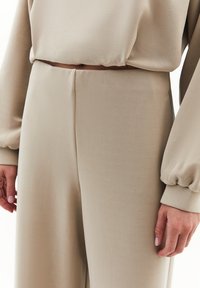 Conjunto de ropa de estar beige que incluye una blusa holgada con mangas abullonadas y pantalones de pierna ancha. Textura suave y lisa con un diseño minimalista.