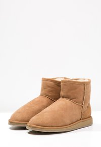 Bottines en suède beige avec doublure en fourrure douce, bout rond et semelle en caoutchouc plate. Des coutures contrastantes parcourent les coutures.