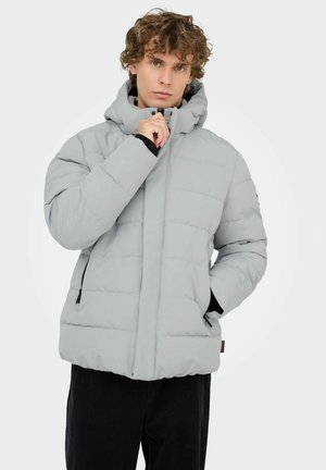 Ljusgrå vadderad jacka med hög krage, dragkedja framtill och två sidofickor; har en slät yta och minimalistisk design.