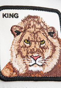 Embroidered patch featuring a lion's face with yellow eyes, detailed fur patterns in brown and tan, bordered with black stitching. Text reads "KING."