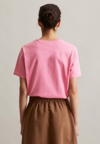 Rosa Baumwoll-T-Shirt mit kurzen Ärmeln und Rundhalsausschnitt, kombiniert mit einem braunen Rock mit elastischem Bund. Schlicht, ohne Muster oder Akzente.