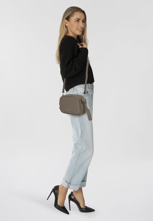 Graue synthetische Umhängetasche mit Reißverschluss, verstellbarem Tragegurt, glatter Textur und einem kleinen Anhänger, getragen mit lässigen hellen Jeans und schwarzen High Heels.