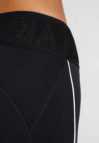 Czarne legginsy sportowe z teksturowanym paskiem w talii i siateczkowym detalem, białym przeszyciem i dopasowanym krojem.