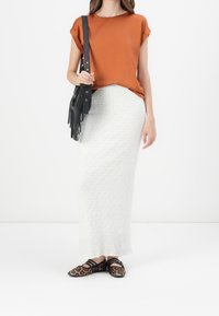Top de manga corta naranja, falda larga de textura blanca y bolso largo con flecos negro. Bailarinas de estampado de leopardo en negro y marrón.