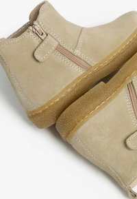 Sandfarbene Wildleder-Ankle-Boots mit einem seitlichen Reißverschluss, strukturiertem Obermaterial, beigem Steppstich und Gummisohle. Doppeldesign mit glatten und rauen Oberflächen.