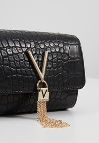 Borsa a mano in pelle nera con texture coccodrillo, con un accento hardware a forma di V in oro e un ciuffo a catena dorata attaccato a un lucchetto.