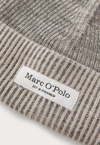 Gorro de punto en gris y beige con canalé vertical, que presenta una etiqueta blanca con texto negro que indica "Marc O'Polo" y "EST. EN ESTOCOLMO."