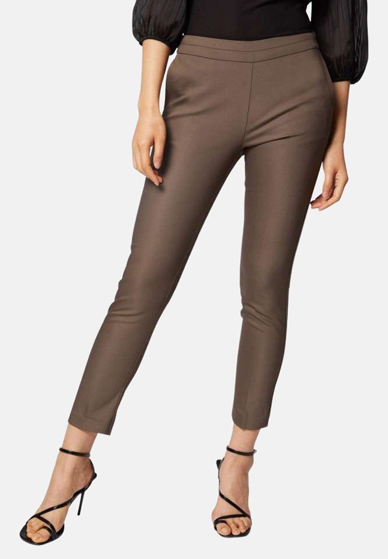 Pantalons marron sur mesure avec une coupe slim, devant plat et longueur cheville courte, associés à des talons hauts noirs à lanières. Texture lisse et détails minimaux.