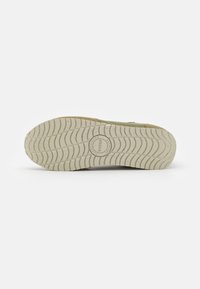 Suola della scarpa con una superficie in gomma testurizzata off-white, caratterizzata da un logo circolare e un motivo a trazione ondulato, con un bordo superiore in suede color marrone chiaro.