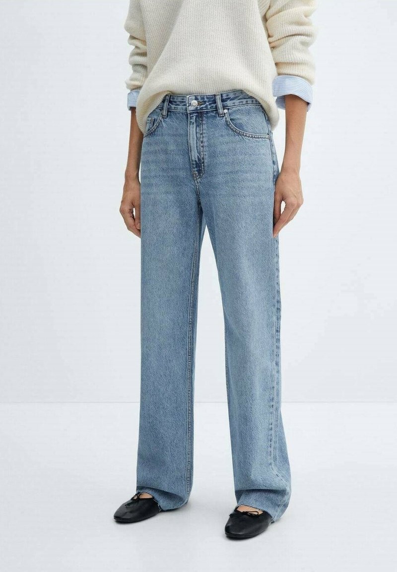 Jeans de tiro alto de pernera recta en azul claro combinados con bailarinas negras y un suéter crema con puños de camisa azul visibles.