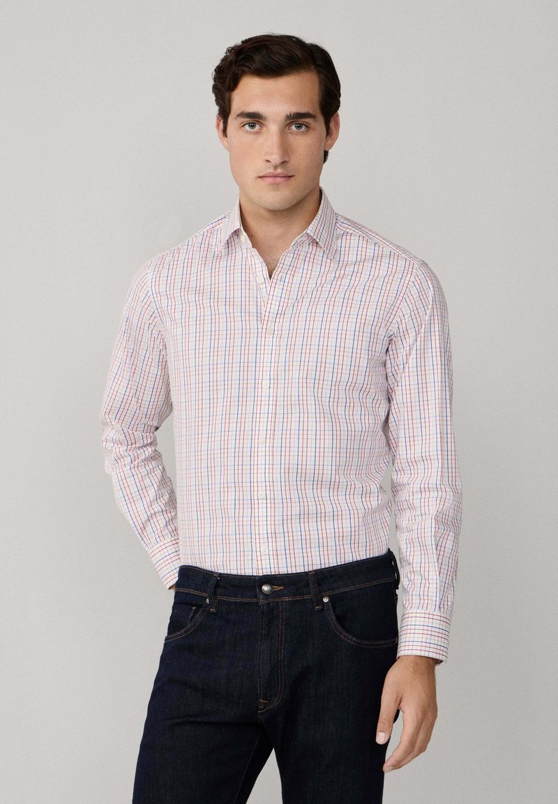 Chemise à manches longues à boutons en tissu de couleur claire, ornée d'un motif à carreaux multicolores, associée à un jean en denim foncé.