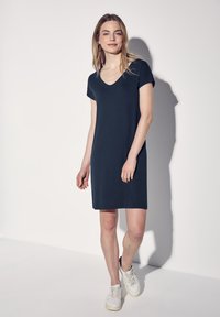 Granatowa, krótko rękawowa sukienka z dekoltem w serek, wykonana z lekkiego materiału, sięgająca tuż nad kolano. Noszona z białymi trampkami.