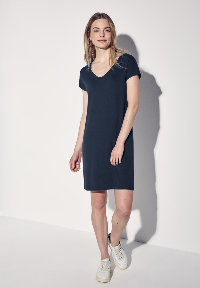 Granatowa, krótko rękawowa sukienka z dekoltem w serek, wykonana z lekkiego materiału, sięgająca tuż nad kolano. Noszona z białymi trampkami.