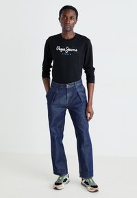 Camisa negra de manga larga con el logo "Pepe Jeans London", combinada con pantalones de mezclilla azul oscuro y zapatillas multicolores.