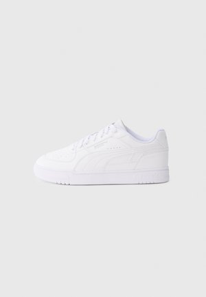 Sneaker bianco Puma low-top con chiusura frontale con lacci e suola testurizzata su sfondo grigio chiaro uniforme.