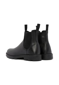 Botas Chelsea de cuero negro con paneles elásticos laterales, suela plana de goma y lengüetas para facilitar el calzado. Textura suave con un brillo sutil.