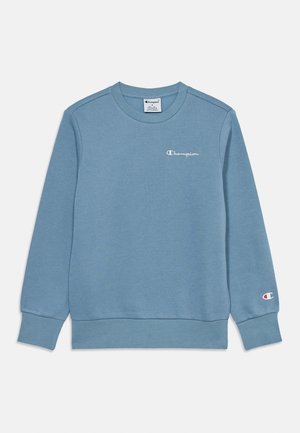 Hellblaues Champion Sweatshirt mit langen Ärmeln und Rundhalsausschnitt, kleines weißes Logo auf der Brust und ein Logopatch am linken Handgelenk.
