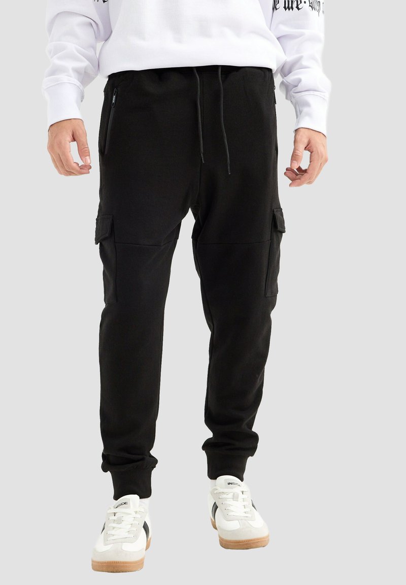 Pantalones jogger negros de mezcla de algodón, con bolsillos laterales con cremallera, cintura elástica con cordón, y puños ajustados. Ajuste regulable.