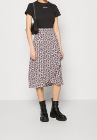 Haut noir à manches courtes avec texte blanc, associé à une jupe midi avec un motif floral en rose et blanc, portée avec des bottes de combat noires.
