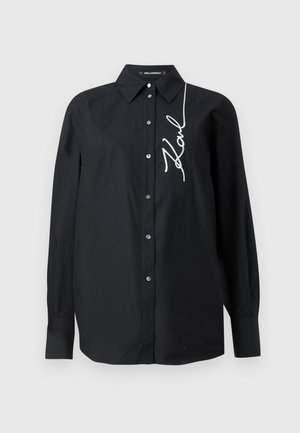 Svart langermet skjorte i bomull, med knappestolsdesign, klassisk krage og en hvit brodert signatur foran.