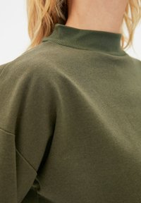Olivgrön höghalstopp i mjuk, slät kvalitet och avslappnad passform. Har vida ärmar och minimalistisk design.