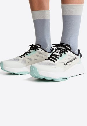 Białe i miętowo-zielone buty sportowe z siateczkową cholewką, czarnymi sznurowadłami i teksturowaną podeszwą, zestawione z jasnoszarymi skarpetami za kostkę.