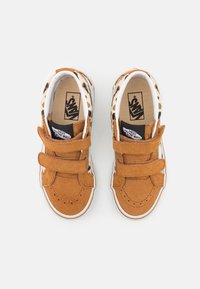Baskets en daim tan avec deux bandes Velcro, semelles en caoutchouc blanc et accents à imprimé léopard autour du col. Logo Vans sur la languette.