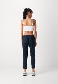 Marineblauwe broek met elastische taille en twee achterzakken, gecombineerd met een witte, aansluitende tanktop. Het model heeft gevlochten haar dat naar achteren is gebonden.
