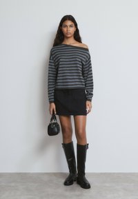 Jersey a rayas negro y gris con hombros descubiertos, mini falda vaquera negra, botas negras hasta la rodilla y un pequeño bolso negro.