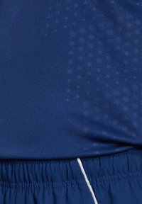 Blauwe sportshirt met een gestructureerde afwerking, voorzien van een subtiel patroon, elastische tailleband en contrasterende witte details op de zoom.