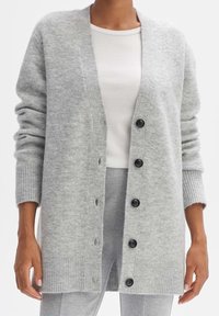 Svetle šedý pletený kardigan s žebrovanými manžetami a spodním lemem, zapínání na knoflíky s černými knoflíky, mírně oversized střih. Měkká textura.