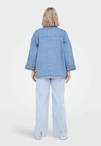 Gaiši zils džinsu žakets ar baltām vertikālām strīpām, pārāk liels izmērs, nokrituši pleci un divas apakšējās pogām aizdarāmas kabatas, saskaņots ar gaiši ziliem džinsiem.