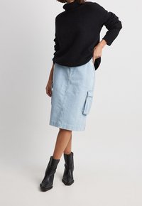 Gonna in denim azzurro chiaro con tasche cargo, abbinata a un maglione nero a maglia e stivali neri alla caviglia. Tessuto morbido con una silhouette aderente.