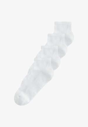 Čtyři bílé kotníkové ponožky s žebrovanými lemy uspořádané přes sebe na bílém pozadí.
