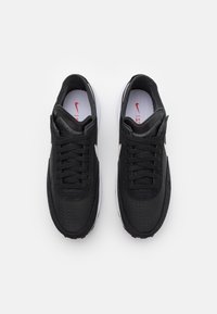 Svarta sportskor med en strukturerad läderöverdel med perforeringar, vita sulor, svarta snören och en liten röd logotyp på innersulan.